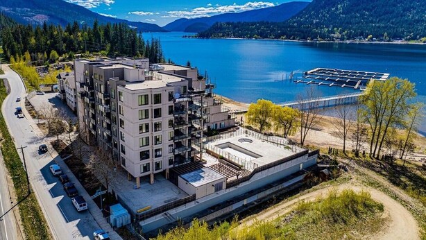 A modern multi-story building with a rooftop terrace, located near a lake with a dock.