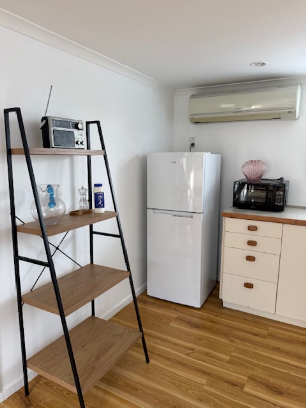 A kitchen with a white refrigerator, a microwave, a shelf with a radio, and a cabinet with drawers.