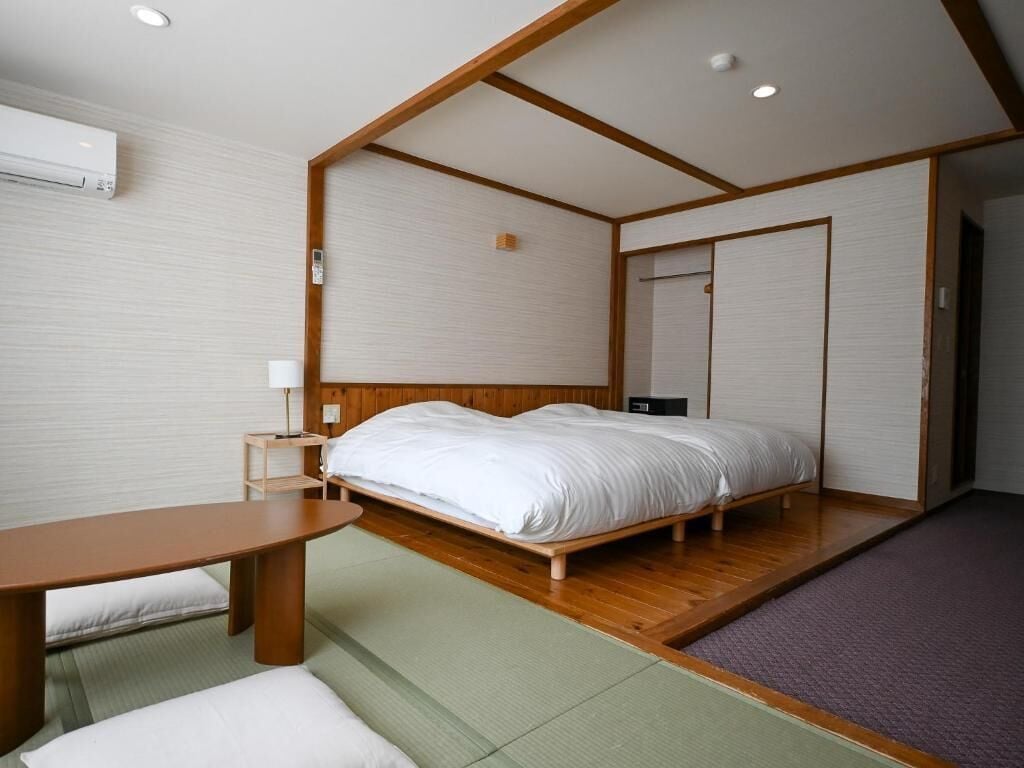 A traditional Japanese-style bedroom with tatami flooring, a wooden bed frame, a small bedside table, and a wall-mounted air conditioning unit.