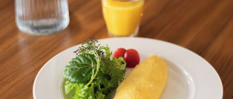 A plate with an omelet, a glass of orange juice, and a bottle of water on a wooden table.
