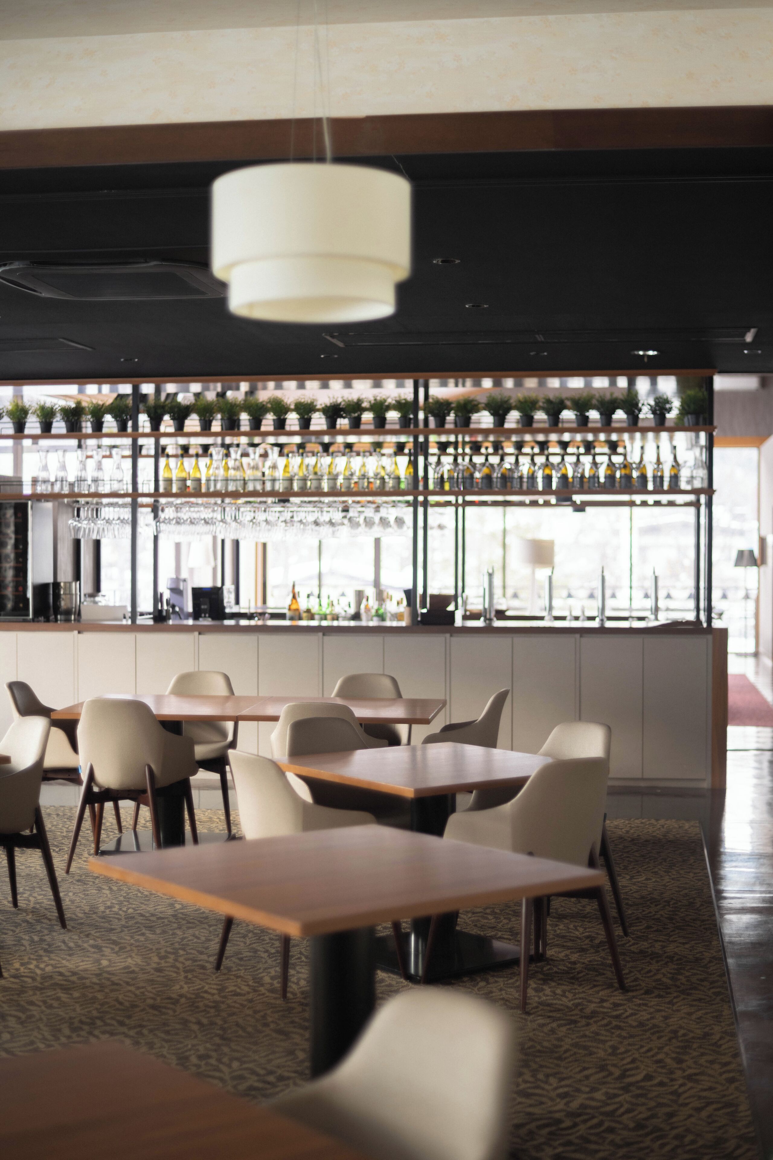 A modern bar area with a long counter, multiple seating options, and a variety of bottles and glasses on display.