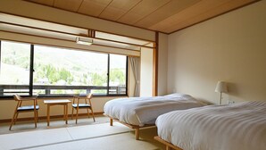 A hotel room with two beds, a window with a view of the outdoors, a table with chairs, and a lamp. - Hotel Goryukan (Hakuba)