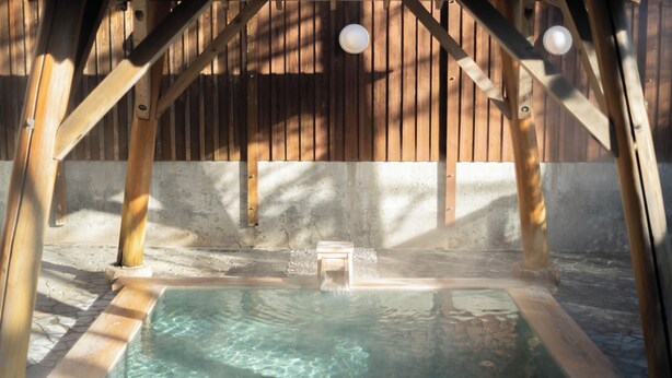 A hot tub in a wooden structure with a concrete floor. - Hotel Goryukan (Hakuba)