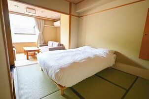 Una habitación con cama, una mesita, una silla y un ventanal con cortinas.