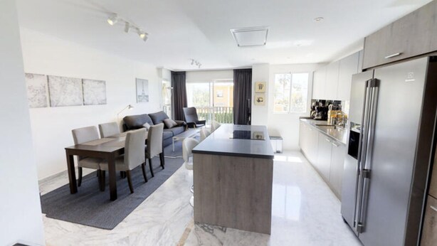 Een moderne keuken met een centraal eiland, een eethoek met tafel en stoelen, en een zithoek met een bank.