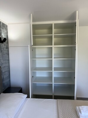 A bedroom with a large white wardrobe, a bed with white bedding, and a grey textured wall. - Elegant Getaway for Couples by the Sea (Sukosan)