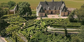 Un edificio grande e histórico con un jardín formal que presenta setos geométricos y un césped central.