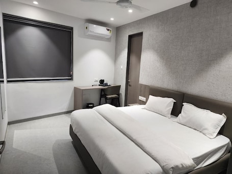 A modern hotel room with a large bed, a desk, a chair, and a window.