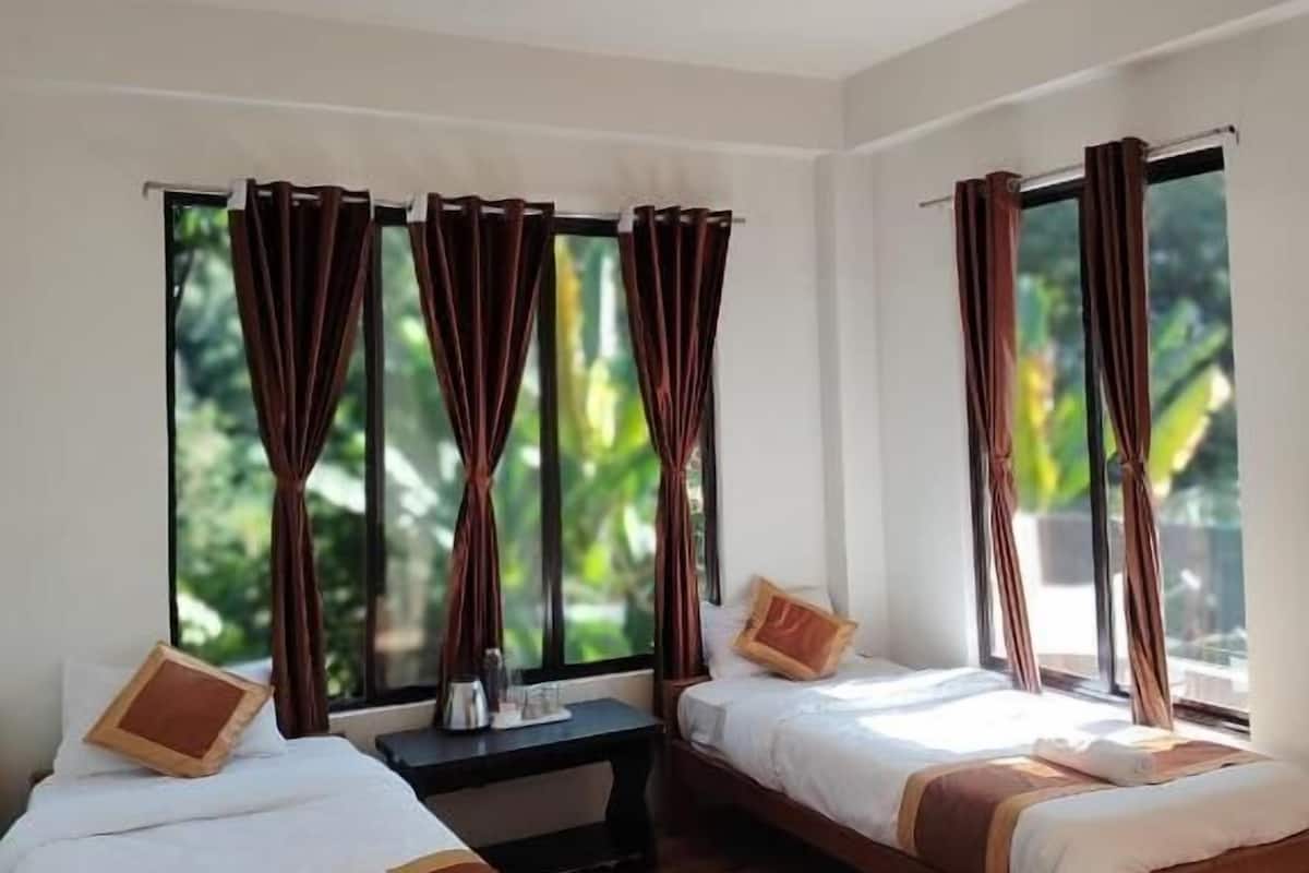 A hotel room with two single beds, a ceiling fan, and large windows with curtains.