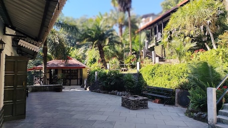 A courtyard with a thatched-roof structure, stone pathway, and lush greenery.