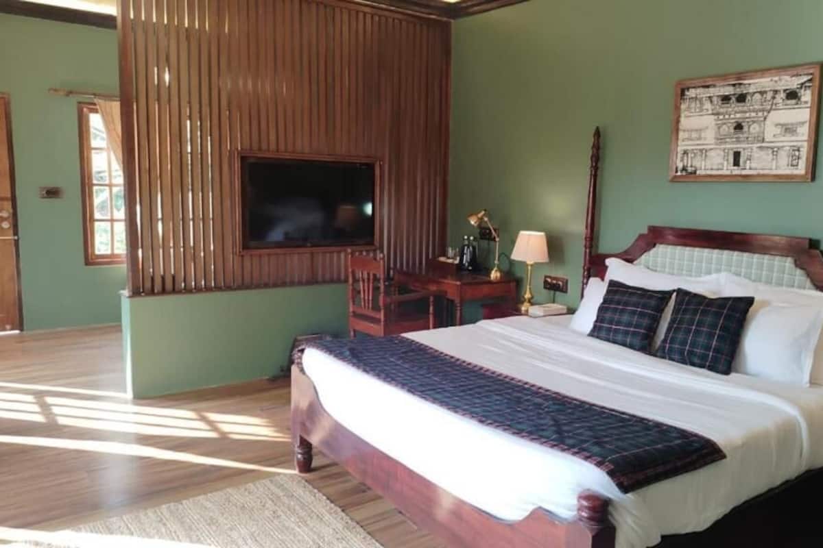 A bedroom with a large bed, a wooden desk, a television mounted on the wall, and a framed picture above the bed.