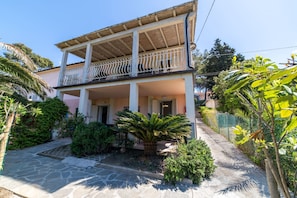 A two-story building with a balcony, surrounded by greenery and a stone pathway. - Appartamenti Procchio - Marina (Marciana)