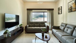 A living room with a sofa, TV, and a view of a cityscape. - Maison Claire Service Villa Wayanad – 4BR Stay Near Attractions (Kottappadi part, Wayand)