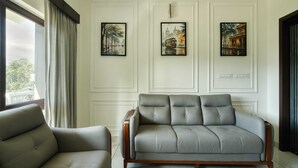 A modern living room with a grey sofa and armchair, white paneled walls, and framed artwork depicting cityscapes. - Maison Claire Service Villa Wayanad – 4BR Stay Near Attractions (Kottappadi part, Wayand)