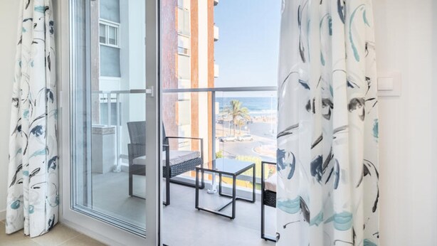 Een balkon met uitzicht op de oceaan en palmbomen, een glazen deur en een tafel met stoelen.
