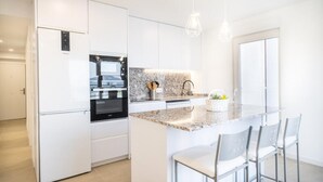 Een moderne keuken met witte kastjes, een inbouwoven, een granieten aanrechtblad en een klein eiland met barstoelen.