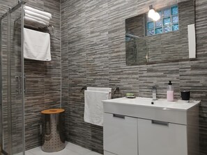 Un bany modern amb plat de dutxa de vidre, un lavabo blanc i un mirall a sobre.
