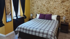 A bedroom with a stone wall, a bed with a plaid bedspread, two bedside tables with lamps, and a mirror on the wall. - Lisbon downtown apartment (Lisboa)