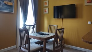 A dining area with a table and chairs, a TV mounted on the wall, and a window with curtains. - Lisbon downtown apartment (Lisboa)