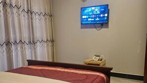 Makuuhuoneessa on sänky, seinälle asennettu televisio, yöpöytä, jossa on puhelin, ja sik-sak-kuvioitu verho.