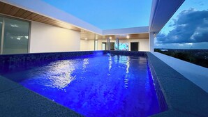 En moderne indendørs swimmingpool med kig til himlen og byens skyline i det fjerne.