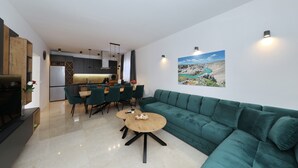 A modern living room with a green sofa, a wooden coffee table, and a dining area with chairs and a table. - Krusevo Pool Villa For 10 (Obrovac)