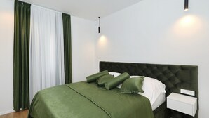 A neatly made bed with a green bedspread and pillows, a white bedside table with a power outlet, and a hanging light fixture. - Krusevo Pool Villa For 10 (Obrovac)