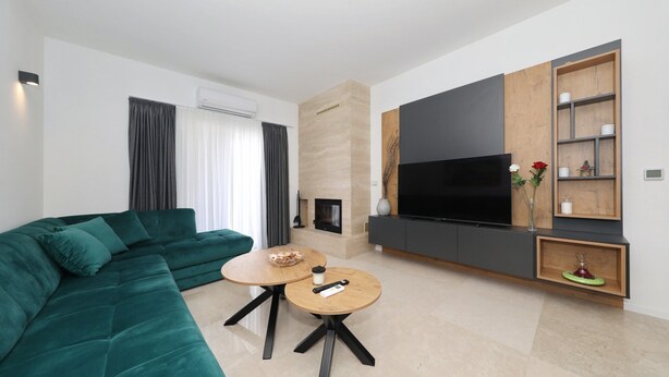 A modern living room with a green sofa, a round wooden coffee table, and a flat-screen TV mounted on a wooden wall. - Krusevo Pool Villa For 10 (Obrovac)
