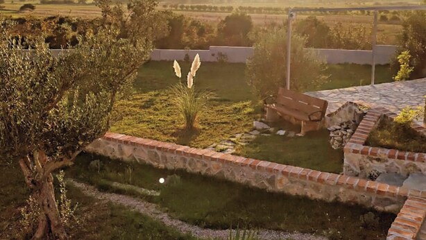 Un jardín con un muro de piedra, un banco y vistas a colinas distantes.