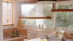 Una cocina con vigas de madera, una isla grande con juego de té y vistas a árboles a través de las ventanas.