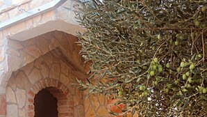 Un área de comedor al aire libre con un arco de piedra, una mesa puesta con platos, vasos y un cuenco, y una planta en maceta cerca.