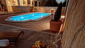 Zona de piscina con una silla de descanso, un frutero y una copa de vino sobre una mesa.