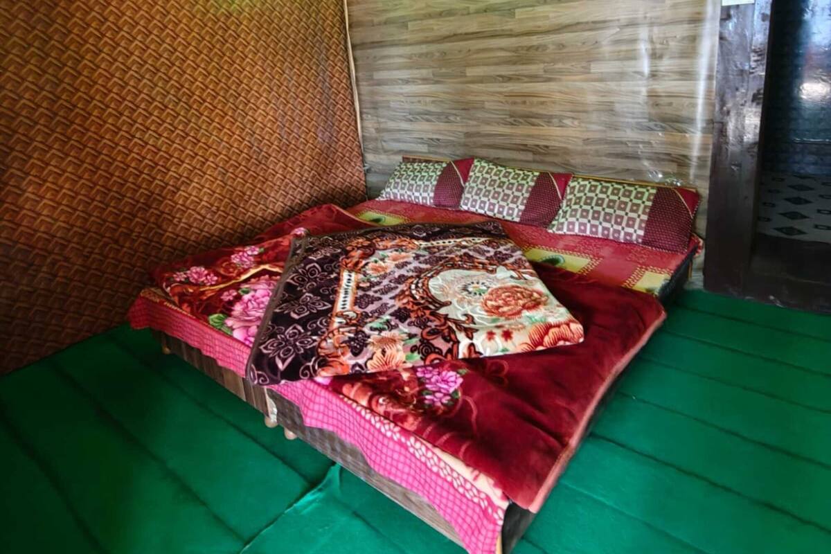 Quarto com teto de madeira, piso verde e cama com colcha estampada.