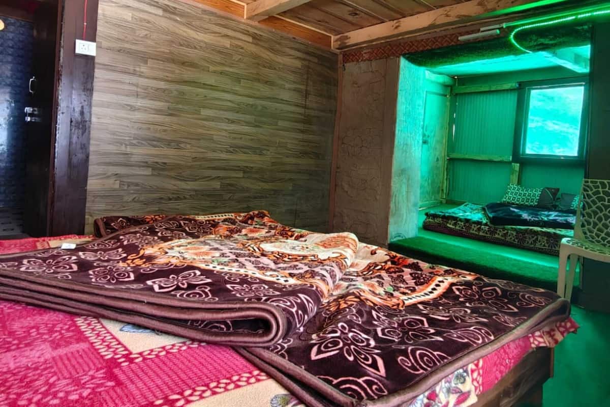 Quarto com teto de madeira, cama com roupa de cama estampada e janela iluminada em verde.