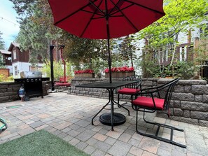 En terrasse med grill, udendørs bord og stole, og en rød parasol.