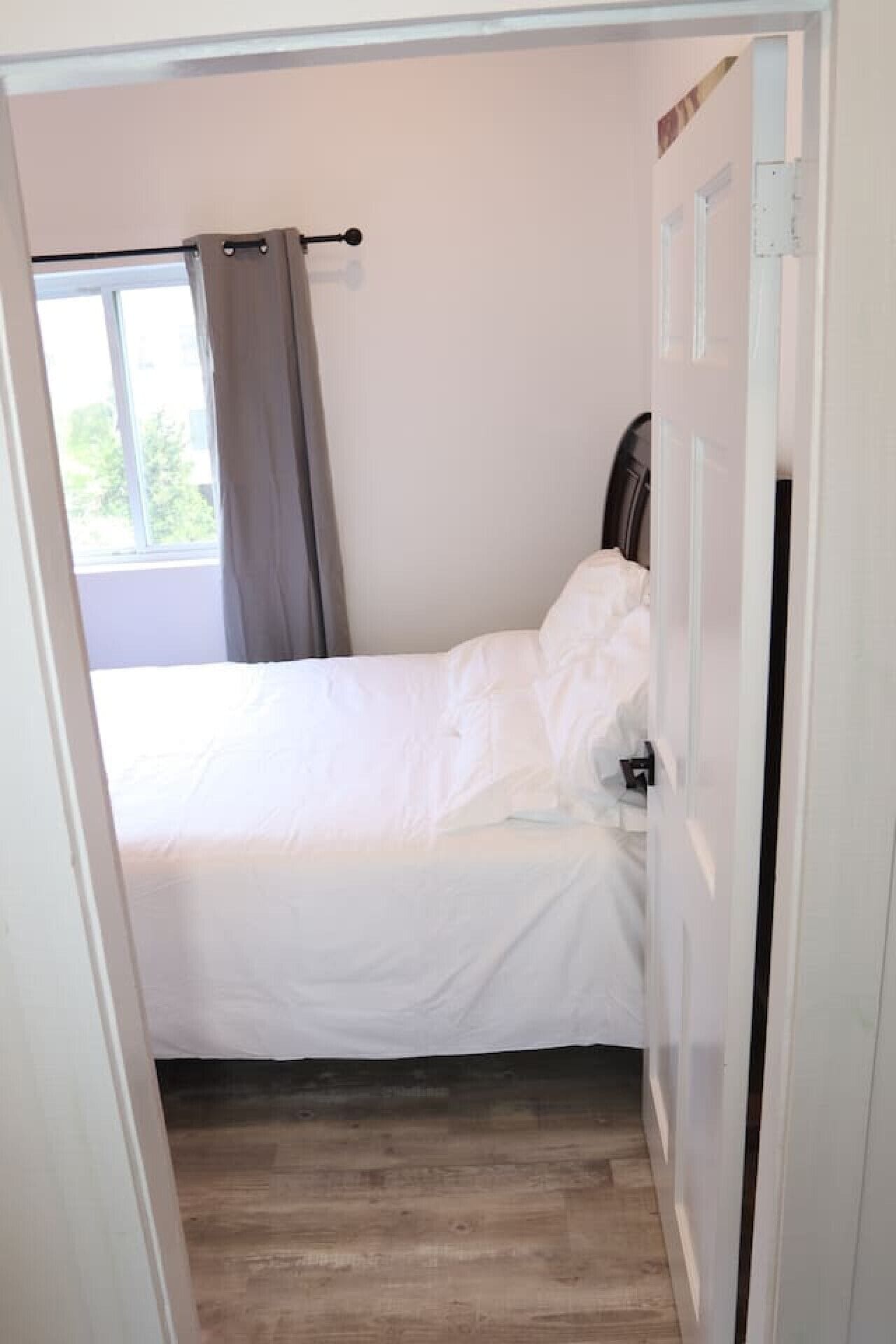 A bedroom with a bed, a window with curtains, and a door.