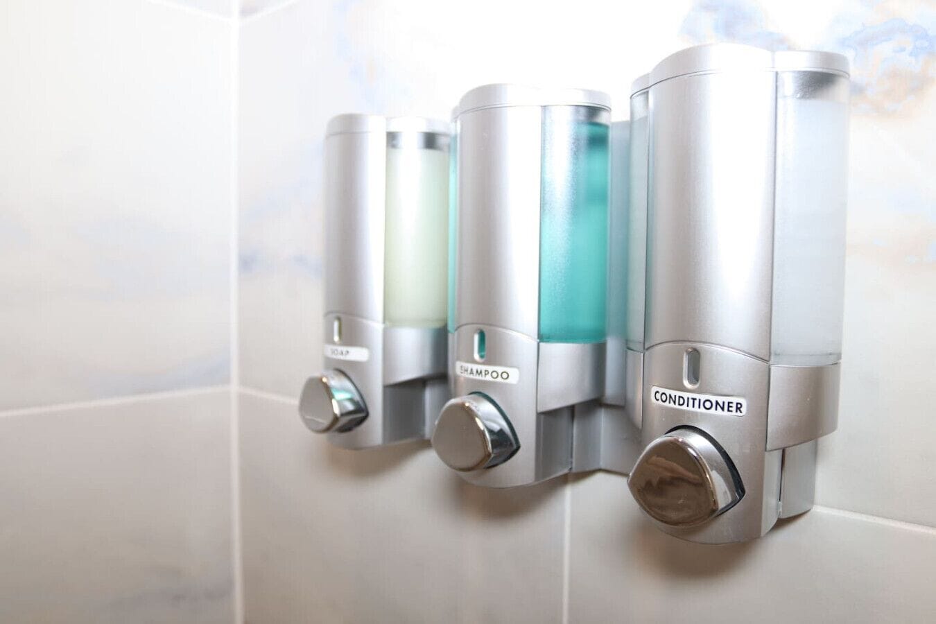 A wall-mounted dispenser with soap, shampoo, and conditioner.