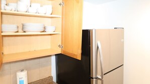 Eine Küche mit einem Holzschrank, einem schwarzen Kühlschrank und einer weißen Flasche auf der Arbeitsfläche.