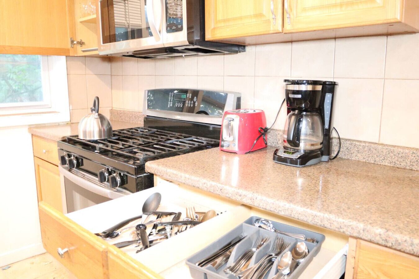 Una cocina con estufa, tostadora, cafetera y cajón con utensilios.
