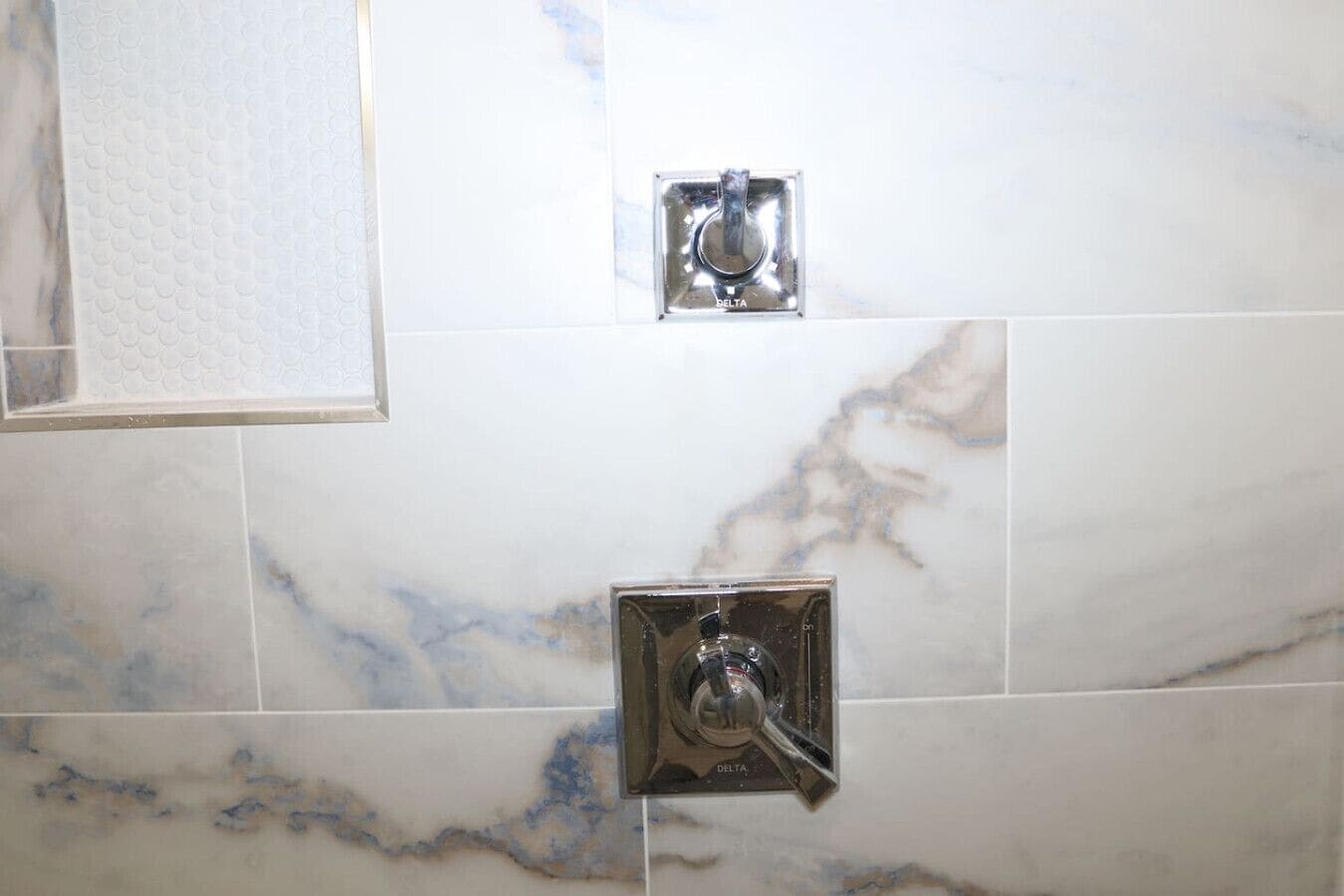 A bathroom with marble tiles, a Delta showerhead, and a Delta faucet.