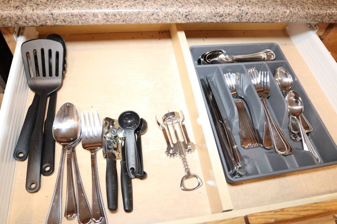 A drawer with kitchen utensils including a spatula, spoon, fork, and various other tools.