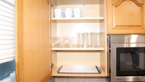 Eine Küche mit Holzausstattung, einem Edelstahlbackofen und Regalen mit weißen Tassen und klaren Gläsern.