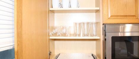 A kitchen with wooden cabinets, a stainless steel oven, and shelves with white mugs and clear glasses.
