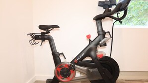 Ein stehendes Fitnessrad mit digitalem Display, platziert in einem Innenraum mit Fenster im Hintergrund.