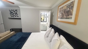 Habitación de hotel con cama, una mesita, una silla, un espejo y un cuadro en la pared.