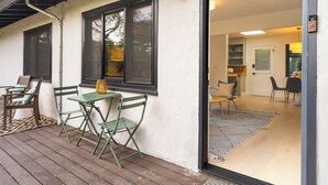 Un espace extérieur abrité, doté d’une table et de chaises, d’une fenêtre et d’une porte donnant sur un espace intérieur avec un tapis et des fauteuils.