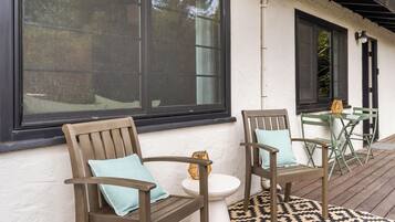 Eine Terrasse mit zwei Holzstühlen, einem kleinen weißen Tisch und einem gemusterten Teppich.
