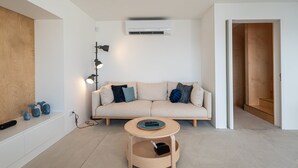 Een moderne woonkamer met een beige bank, een ronde houten salontafel en een wandairconditioner.