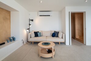 A modern living room with a beige sofa, a round wooden coffee table, and a wall-mounted air conditioner. - The Lookout | Private Beach Access (São Roque)