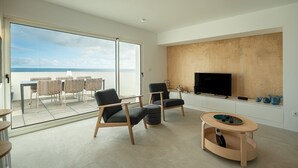 Een moderne woonkamer met een grote schuifglazen deur die leidt naar een balkon, een flatscreen televisie bevestigd aan een houten wand, en een klein rond tafeltje met een laptop erop.